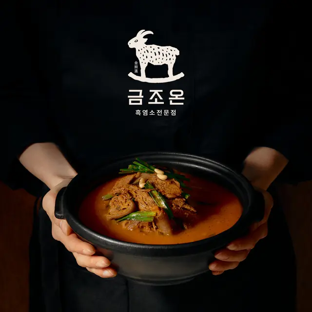 금조온 로고가 새겨진 앞치마 앞으로 두 손에 받쳐 든 여의도 흑염소 탕